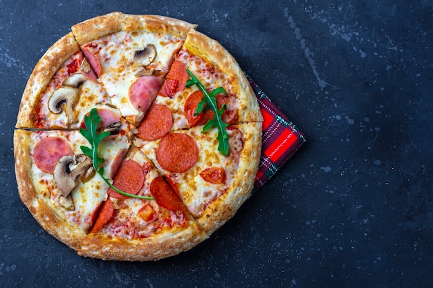 Una pizza fresca preparata con salame, funghi, prosciutto e formaggio su uno sfondo scuro. Pranzo o cena tradizionali italiani. Concetto di fast food e cibo di strada. Flat ly, vista dall'alto