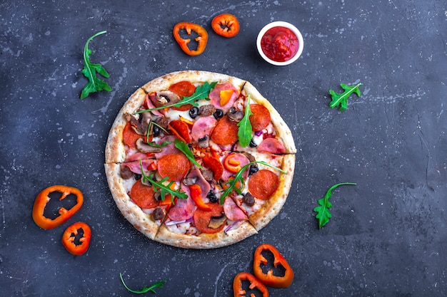 Una pizza fresca preparata con salame, funghi, prosciutto e formaggio su uno sfondo scuro. Pranzo o cena tradizionali italiani. Concetto di fast food e cibo di strada. Flat ly, vista dall'alto