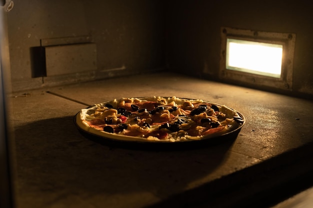 Una pizza grande e rotonda viene cotta in forno con luce. Il formaggio si sta sciogliendo. Pizzeria.