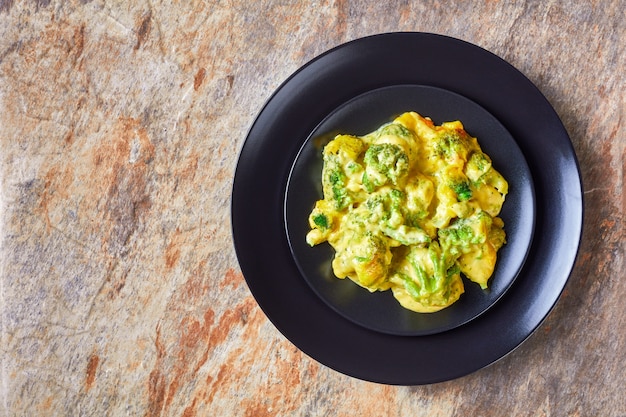 Una porzione di formaggio di broccoli cuocere, casseruola di broccoli su una piastra nera su un tavolo, vista orizzontale dall'alto, piatto, spazio libero