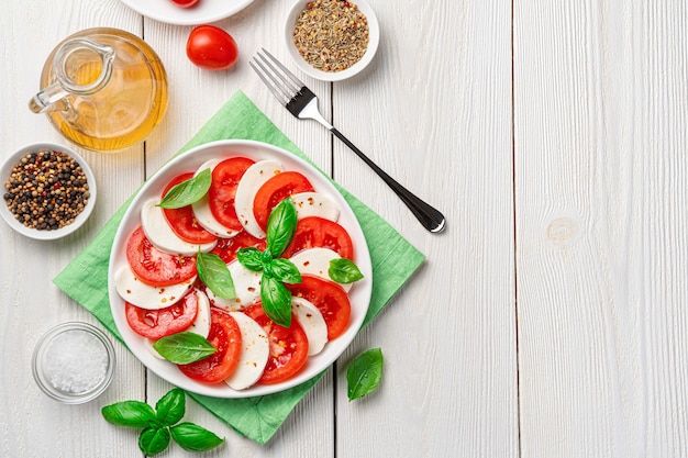 Una porzione di insalata caprese con pomodoro e mozzarella su sfondo bianco. Cibo italiano.