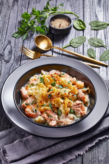 Una porzione di torta di salmone con eglefino affumicato, gamberi, spinaci, condita con purè di patate in una ciotola, cucina inglese