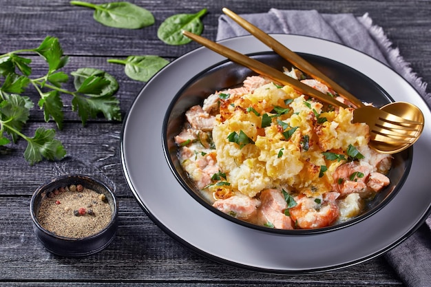 Una porzione di torta di salmone con eglefino affumicato, gamberi, spinaci, condita con purè di patate in una ciotola, cucina inglese