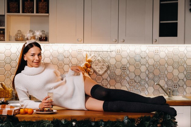 Una ragazza a Natale è sdraiata sul tavolo della cucina e tiene in mano un bicchiere di champagne. Donna alla vigilia di capodanno con champagne