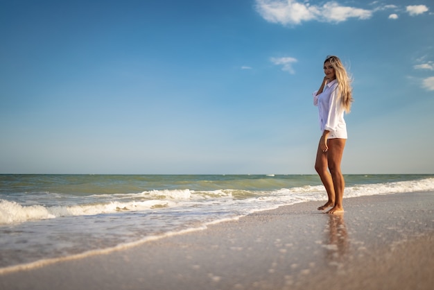 Una ragazza abbronzata in costume da bagno blu e maglietta leggera si gode l'estate al mare