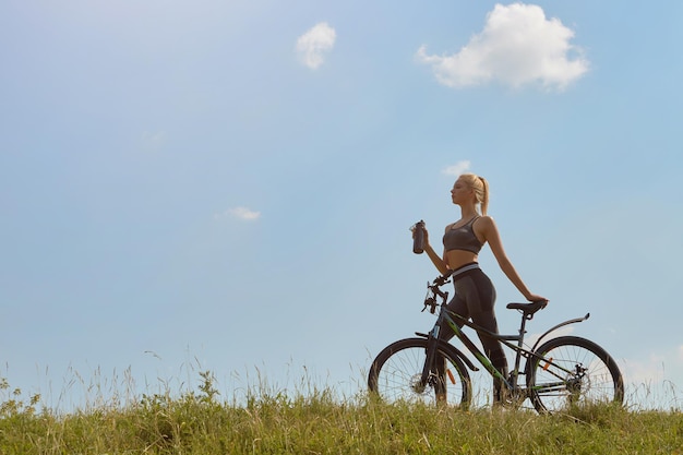 Una ragazza accanto a una bicicletta beve acqua sullo sfondo della natura