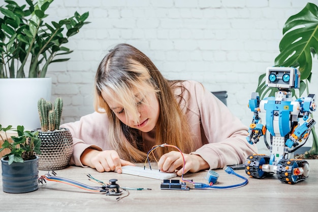 Una ragazza adolescente che collega i cavi ai chip dei sensori mentre impara la codifica e la robotica arduino