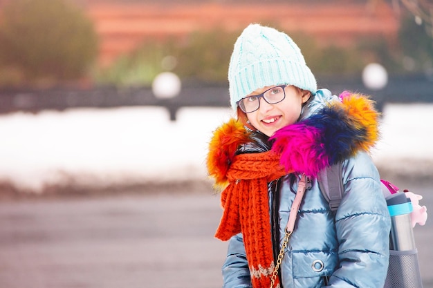 Una ragazza adolescente con gli occhiali un cappello blu e una giacca in caso di neve Ritratto invernale di una studentessa