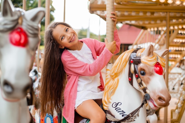 Una ragazza adolescente con i capelli lunghi rotola su una giostra di cavalli altalena. Seduto su un cavallo in un parco di divertimenti