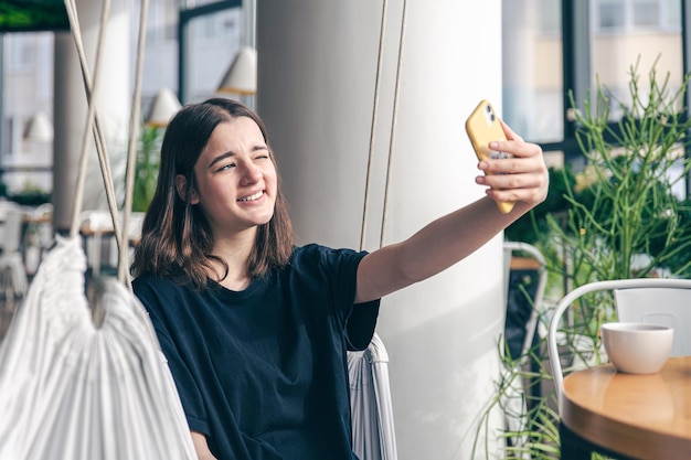 Una ragazza adolescente si siede su un'amaca sospesa e si fa un selfie su uno smartphone