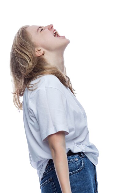 Una ragazza adolescente urla Giovane bella bionda in una maglietta bianca e jeans Depressione e orrore isolato su sfondo bianco Verticale Vista laterale