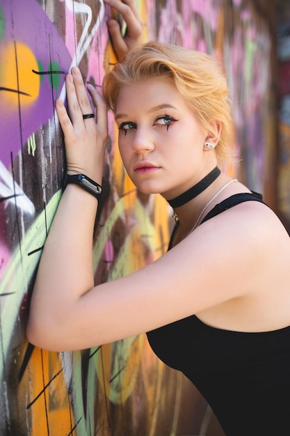 Una ragazza alla moda con una brillante acconciatura corta e un trucco candido posa sullo sfondo di un muro di graffiti