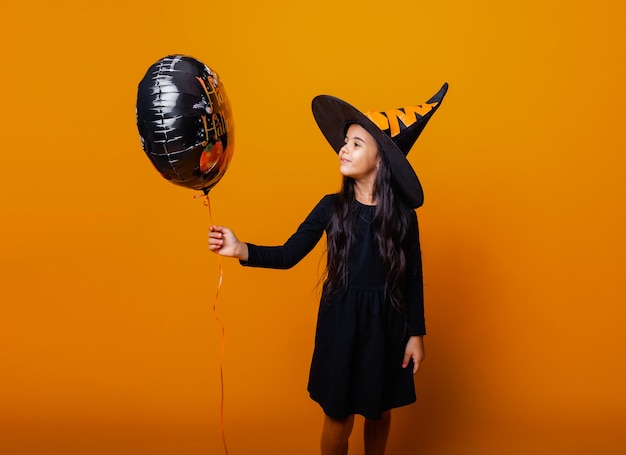 Una ragazza allegra in costume da strega tiene in mano un palloncino con la scritta Halloween. concetto di halloween.