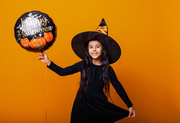 Una ragazza allegra in costume da strega tiene in mano un palloncino con la scritta Halloween. concetto di halloween.