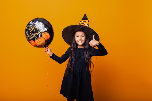 Una ragazza allegra in costume da strega tiene in mano un palloncino con la scritta Halloween. concetto di halloween.