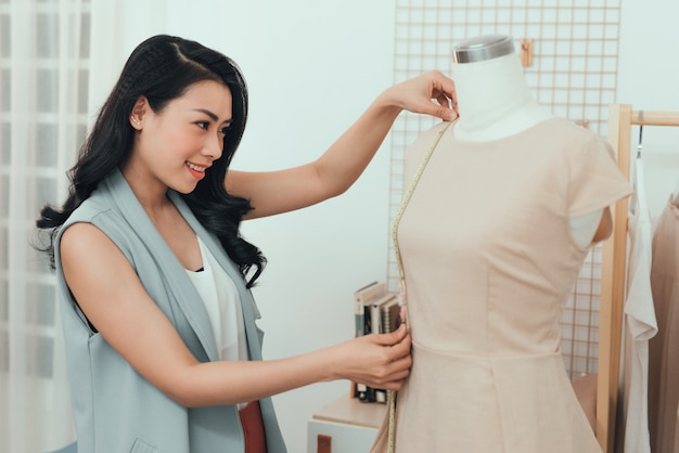 Una ragazza asiatica sta lavorando nello studio dell'officina. Si adatta al vestito sul manichino.