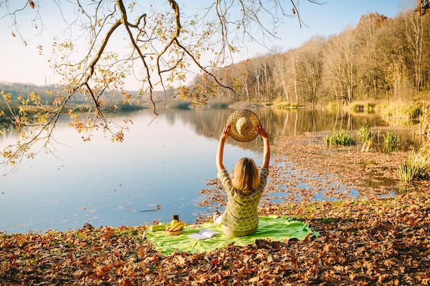 Una ragazza attraente si siede da sola su una foglia gialla con una vista meravigliosa di un lago e montagne Una donna gode di un posto pittoresco Il concetto di riposo e relax