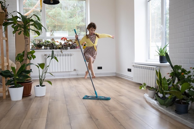 Una ragazza balla con lo spazzolone per pulire il pavimento in una casa nuova pulizia generale in una stanza vuota la gioia di muoversi aiuta nelle faccende domestiche