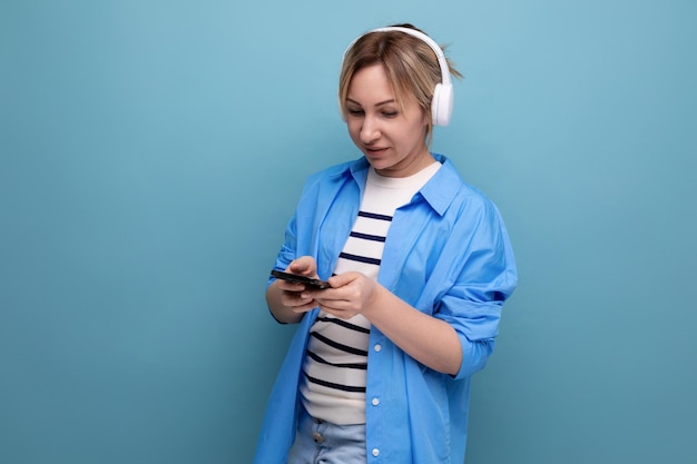 Una ragazza bionda brillante vestita con una camicia casual ascolta musica nell'applicazione in modalità wireless