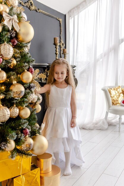 Una ragazza bionda carina decora un albero prima di Natale a casa. Infanzia felice. Decorare un albero di Natale prima di Natale.