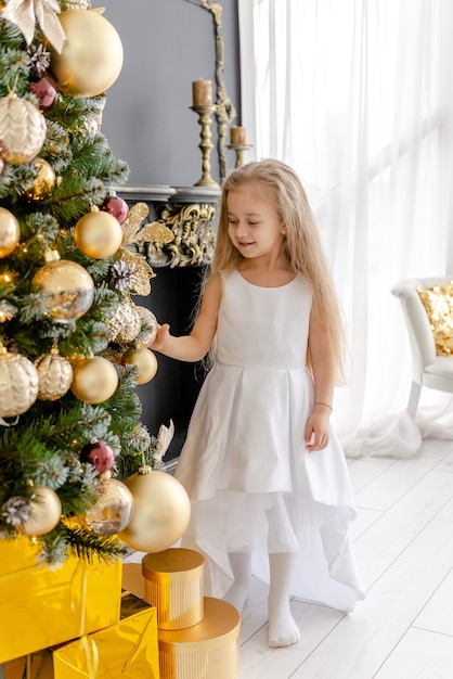 Una ragazza bionda carina decora un albero prima di Natale a casa. Infanzia felice. Decorare un albero di Natale prima di Natale.