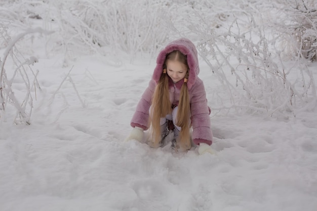 una ragazza bionda con i capelli lunghi in una pelliccia rosa è seduta in un parco invernale innevato