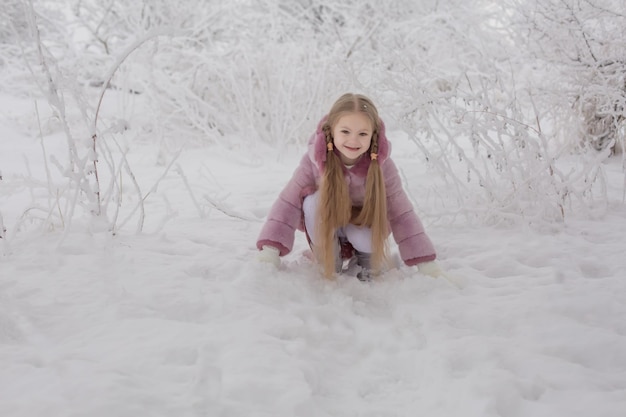 una ragazza bionda con i capelli lunghi in una pelliccia rosa è seduta in un parco invernale innevato