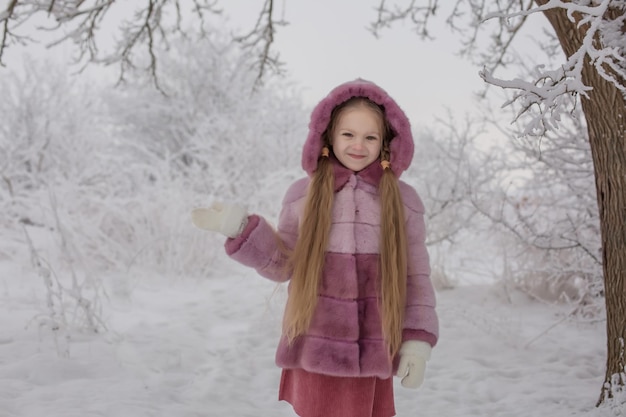 una ragazza bionda con i capelli lunghi in una pelliccia rosa in un parco invernale innevato