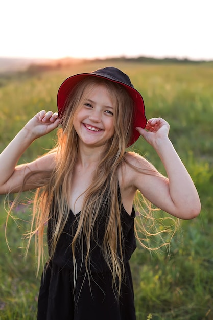 una ragazza bionda con un abito nero e un cappello panama nero si trova sotto i raggi del sole al tramonto