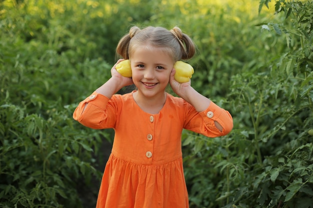 Una ragazza bionda con un vestito arancione sta in giardino e tiene in mano un peperone