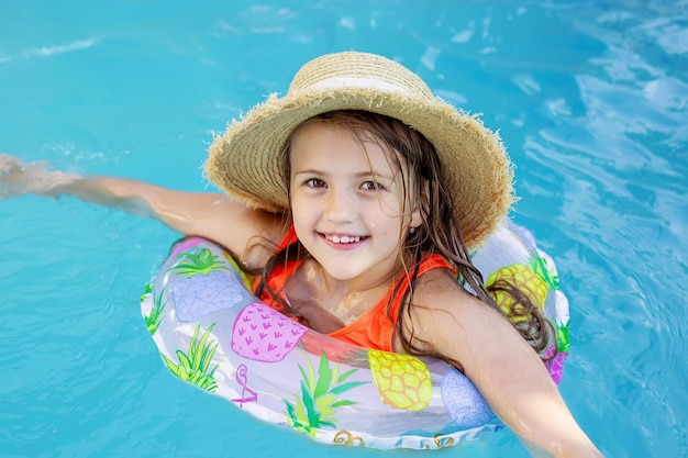 una ragazza bionda felice con un cappello di paglia e una balestra di salvataggio sta nuotando in piscina