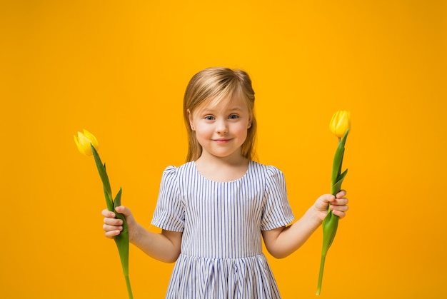 Una ragazza bionda felice tiene due tulipani su colore giallo