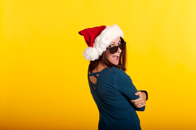Una ragazza bruna che indossa un cappello di Babbo Natale con uno sfondo giallo e occhiali da sole