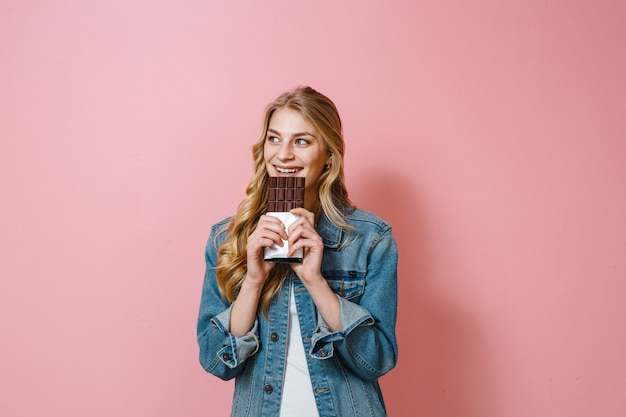 Una ragazza bruna con il cioccolato in mano che profuma di sapore su uno sfondo rosa