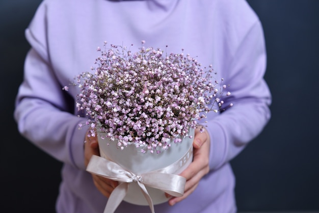 Una ragazza bruna in una delicata felpa viola tiene un bouquet tra le mani.