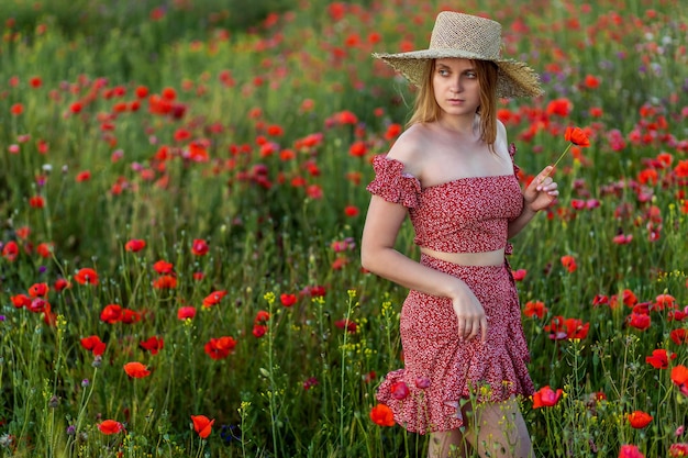 Una ragazza cammina in un campo di papaveri. In un vestito rosso e un cappello di paglia.