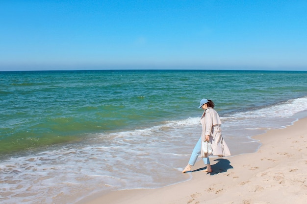 Una ragazza cammina lungo la riva del mare blu sull'atmosfera estiva della spiaggia sabbiosa