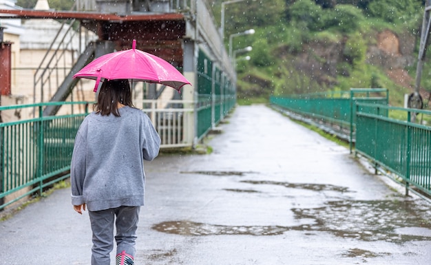 Una ragazza cammina sotto un ombrello in caso di pioggia su un ponte nella foresta