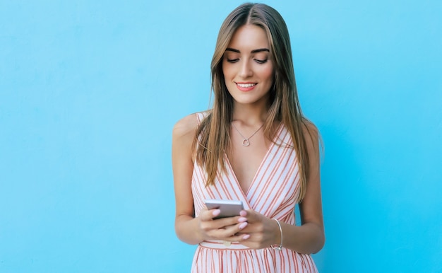 Una ragazza carina con i capelli lunghi e biondi sta scrivendo qualcosa sul suo telefono, mentre guarda lo schermo e sorride