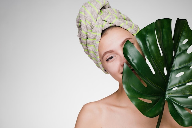 Una ragazza carina con un asciugamano in testa tiene una foglia verde, gode di una spa