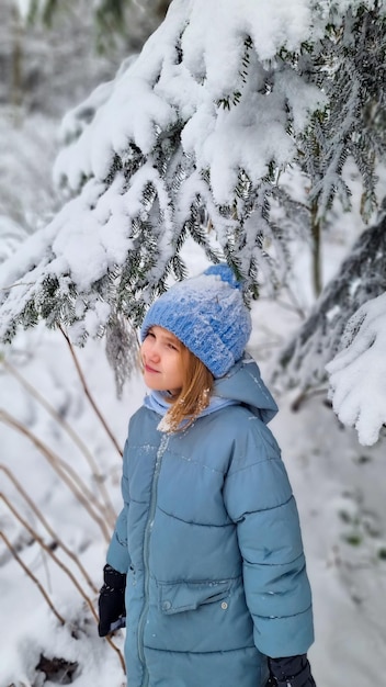 Una ragazza carina con un cappotto blu sotto un abete rosso innevato