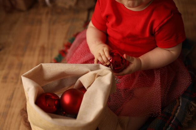 una ragazza carina con un costume natalizio rosso tira fuori i giocattoli dell'albero di Natale da una borsa con regali