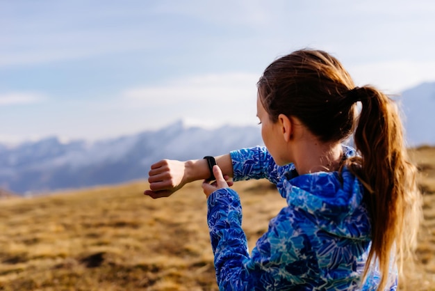 Una ragazza carina con una giacca blu viaggia attraverso le montagne del Caucaso, guarda il tempo con un orologio da polso