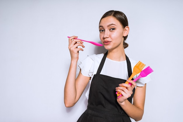 Una ragazza carina cuoca in grembiule nero tiene in mano gli elettrodomestici da cucina