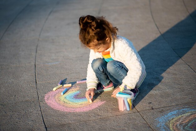 Una ragazza carina disegna un arcobaleno con i pastelli per strada Creation Kids Street