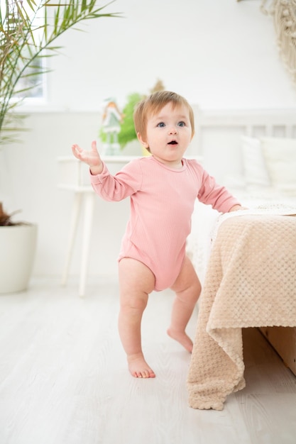 Una ragazza carina e sana è in piedi accanto al letto nella camera da letto a casa i primi passi del bambino il bambino sta imparando a camminare