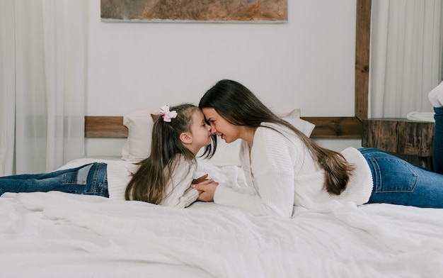 Una ragazza carina e sua madre si stanno godendo una mattinata di sole. Divertiti a casa. La famiglia sta giocando sul letto in camera da letto.