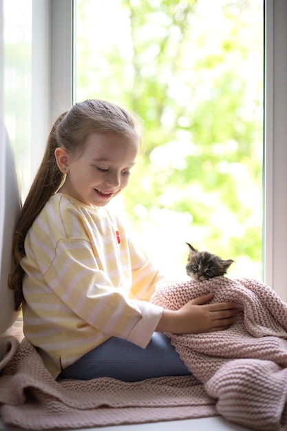 Una ragazza carina gioca con il suo gattino soffice seduto sul davanzale della casa Amicizia con un animale domestico Stile di vita