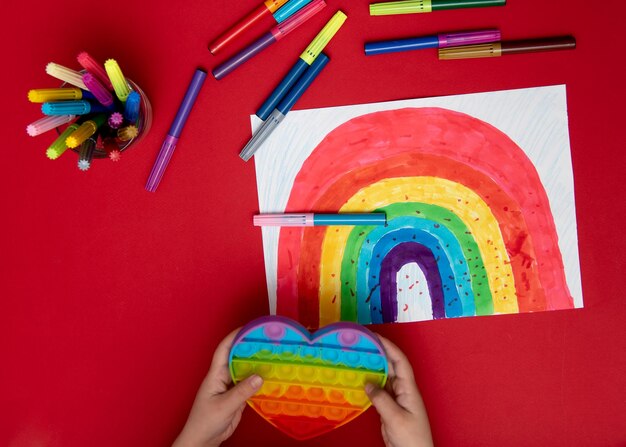 Una ragazza carina in abiti arcobaleno disegna un arcobaleno con pennarelli multicolori House Childhood