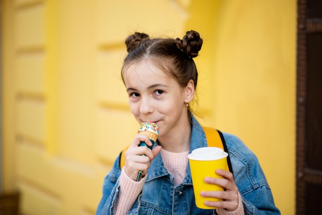 Una ragazza carina mangia il gelato e beve il tè all'esterno Infanzia da asporto Il concetto di cibo delizioso